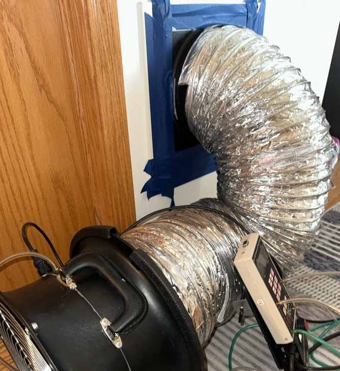 Duct blaster connected to a wall register with painter's tape during a duct leakage test