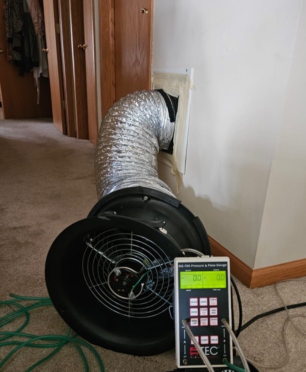 Duct blaster fan and DG-700 pressure gauge set up in a hallway for a duct leak test
